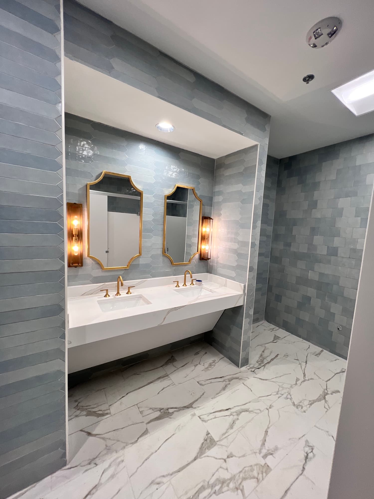 Completed commercial restroom with blue feature tile, double vanity, and large-format floor tile
