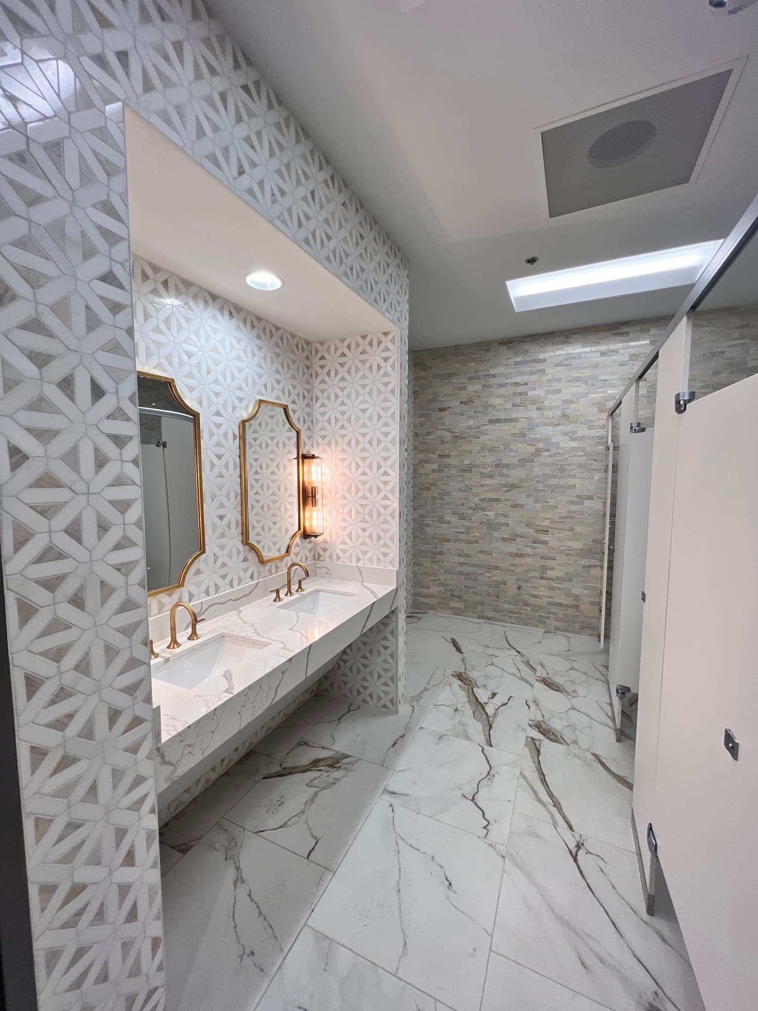 Completed commercial restroom with decorative geometric wall tile and marble-look floor tile