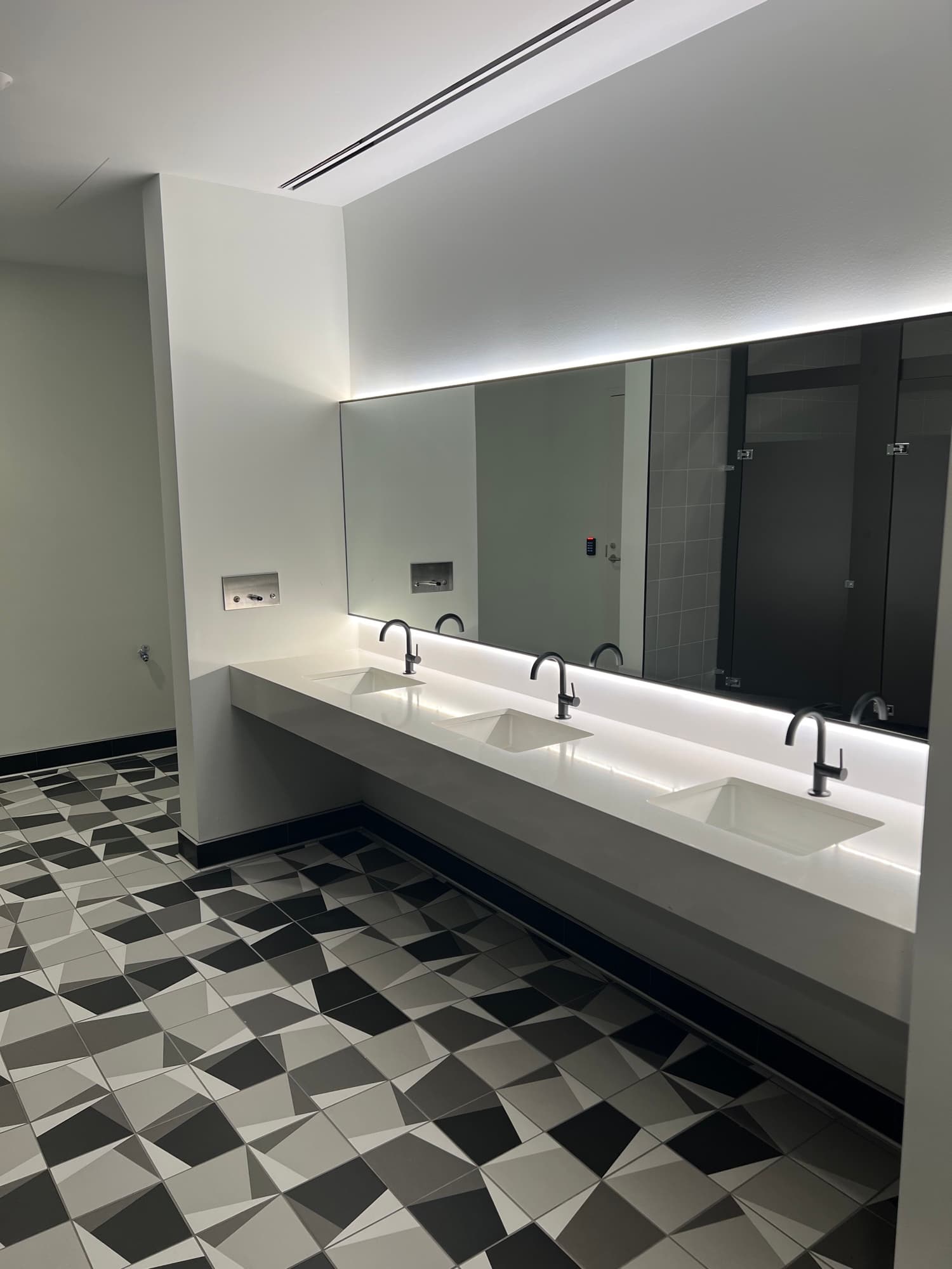 Completed commercial washroom with a geometric tile floor, dark shower walls, and illuminated vanity