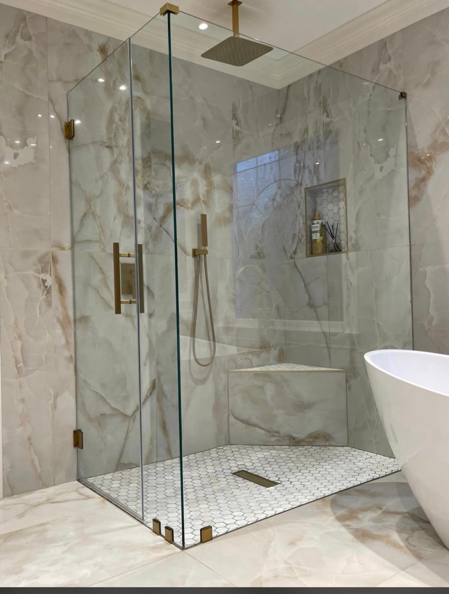 Completed residential shower with gold-toned fixtures, a glass enclosure, and mosaic shower floor