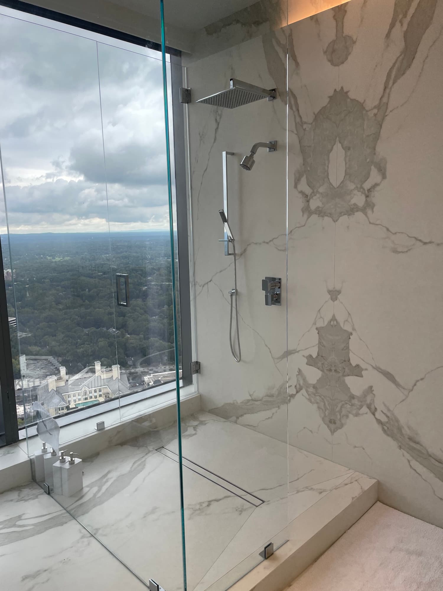 Completed glass shower with book-matched large-format marble-look wall surfaces and a city view
