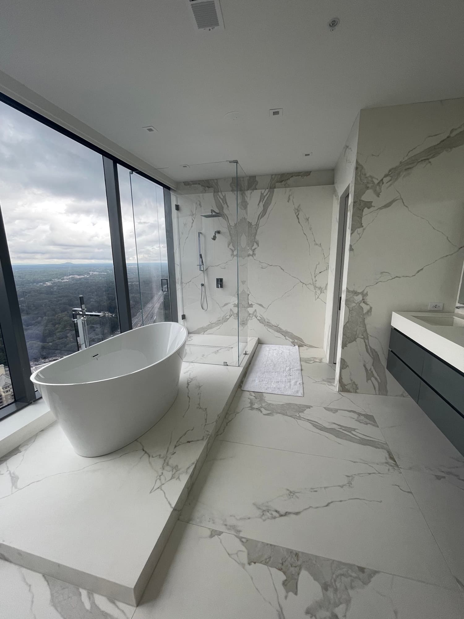 Completed high-rise bathroom with large-format marble-look surfaces, a glass shower, and a freestanding tub