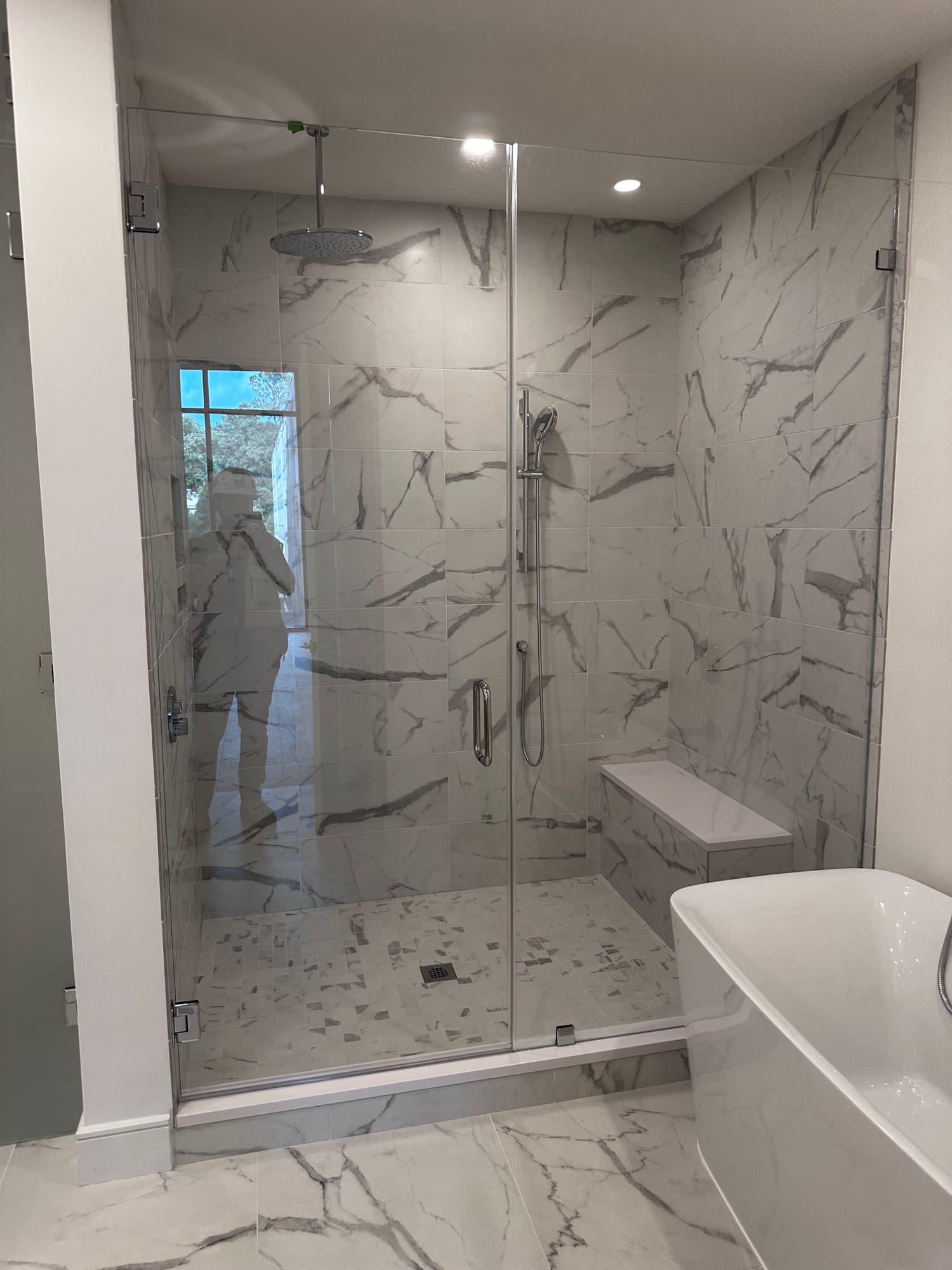 Completed residential bathroom with a glass-enclosed marble-look shower and coordinated floor tile