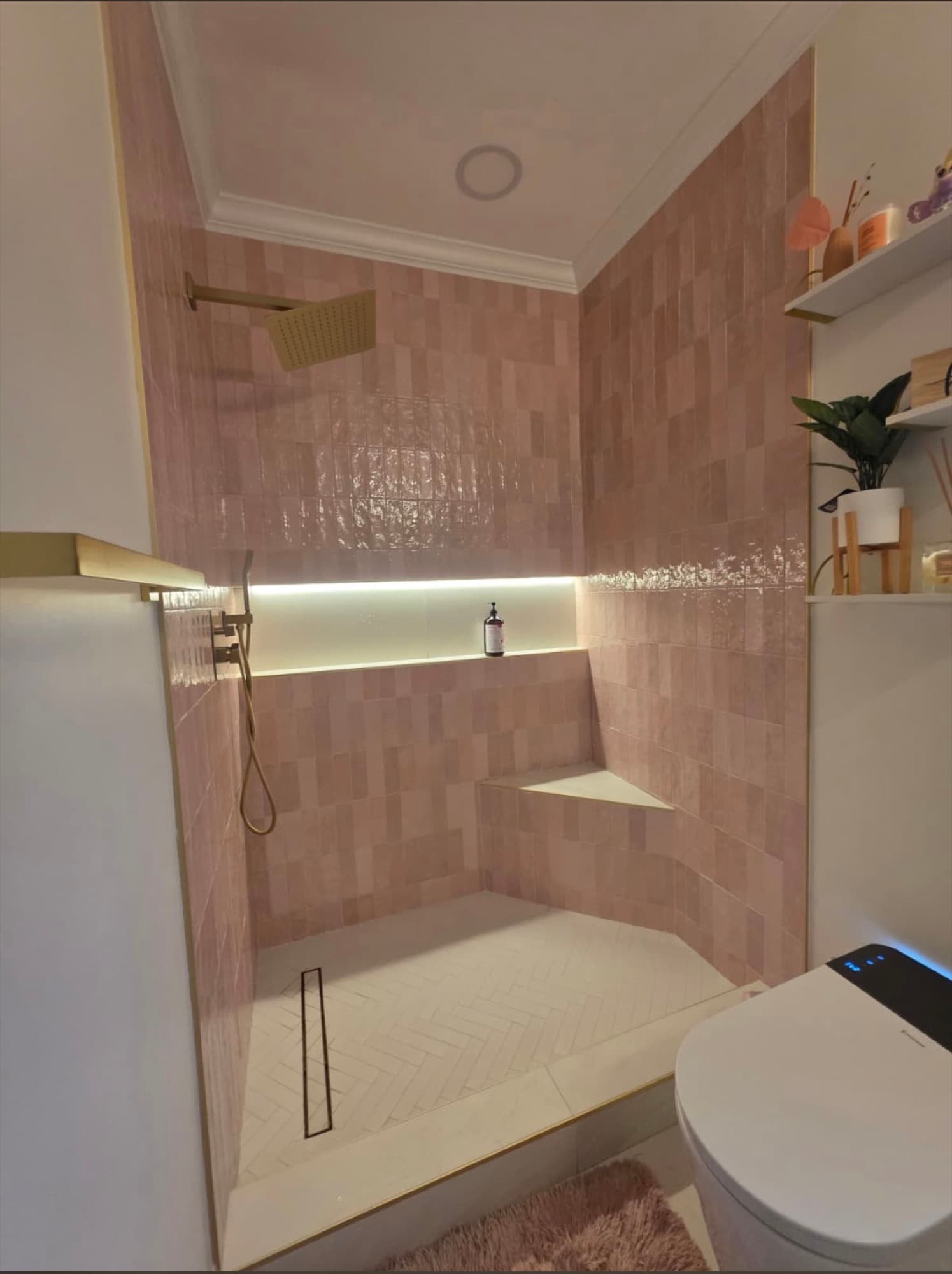 Completed residential shower with soft pink wall tile, a lit recessed niche, and a patterned shower floor