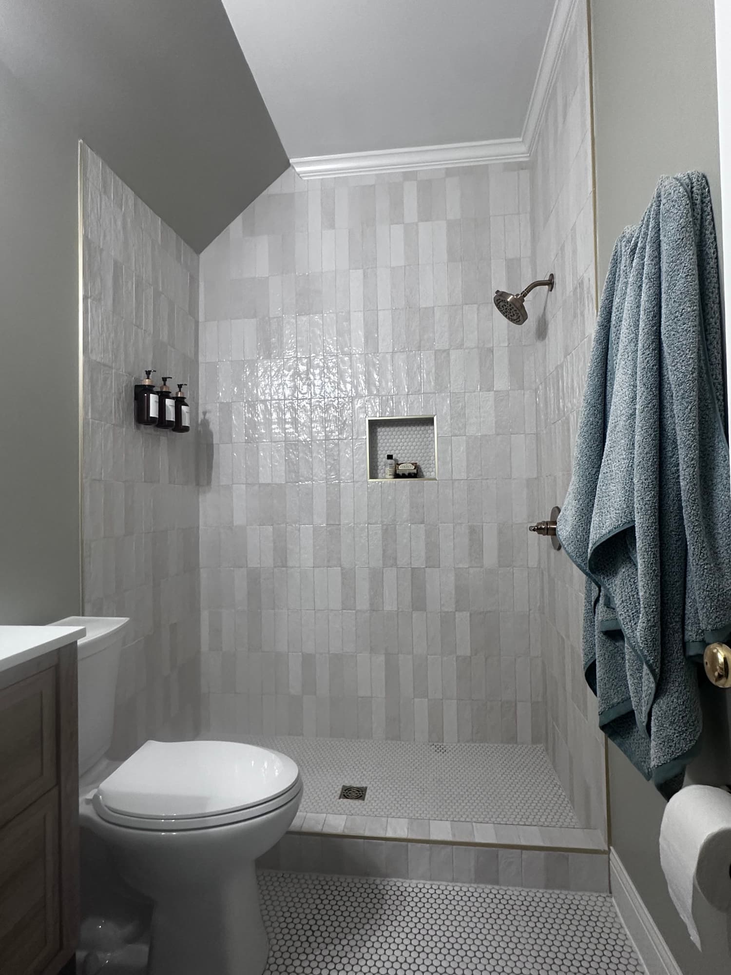 Completed residential shower with textured white wall tile, mosaic flooring, and a recessed niche
